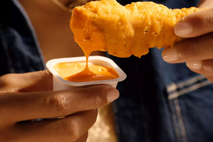 Close-up of a person dipping a McDonald's chicken strip into orange sauce.
