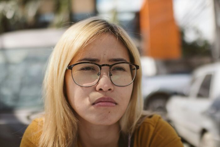 Young woman with glasses looking frustrated outdoors, illustrating relationship arguments that feel like sitcom material.