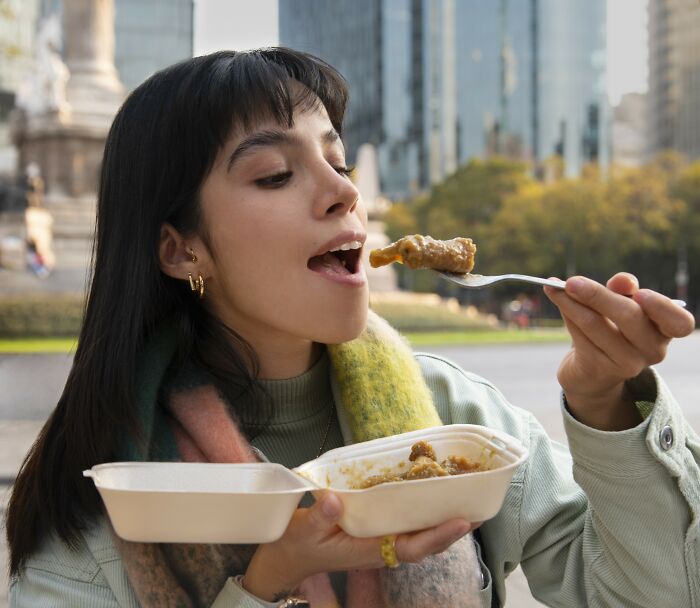 Person in a city setting eating from a takeout container, highlighting everyday things that seem harmless.