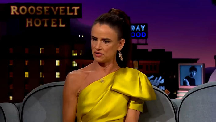 Person in a yellow dress speaks on a talk show with Roosevelt Hotel in the background, discussing celebrity encounters.