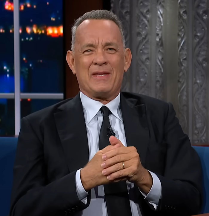 Celebrity encounter on talk show, man in black suit and tie, expressing emotion.