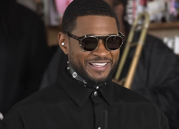 Man in sunglasses smiling, wearing a black shirt, during a music performance.