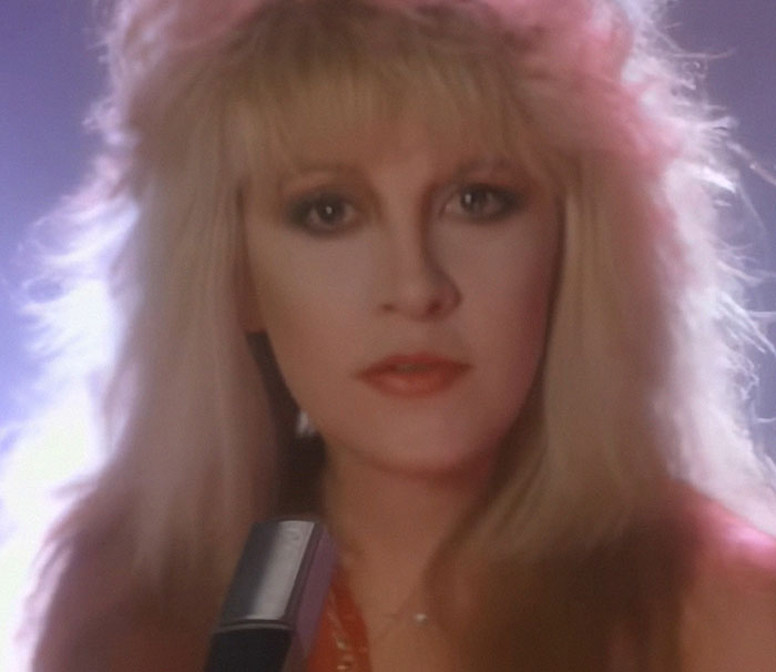 Blonde woman with intense gaze holding a microphone, bathed in soft lighting, epitomizing celebrity encounters.