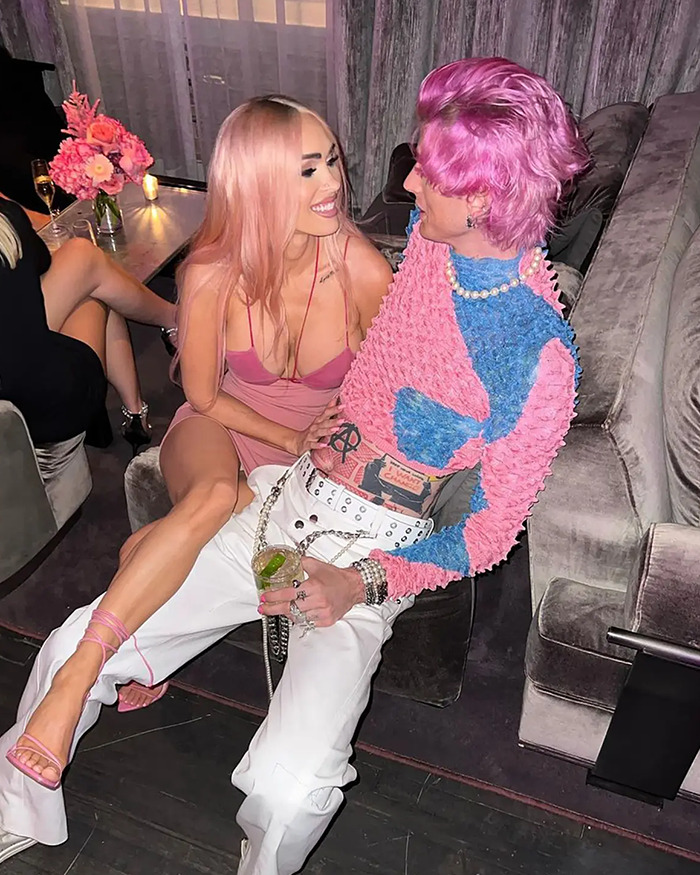 Couple with pink hair and outfits sitting closely, sharing a moment in a stylish lounge.