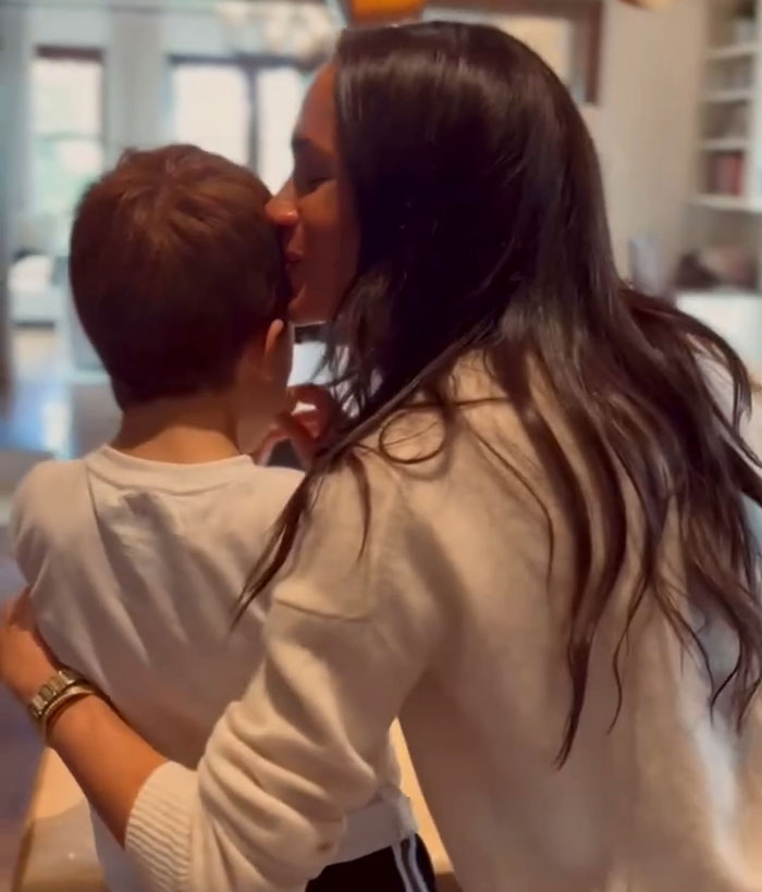 Woman in a white sweater gently hugs a child in a casual indoor setting.