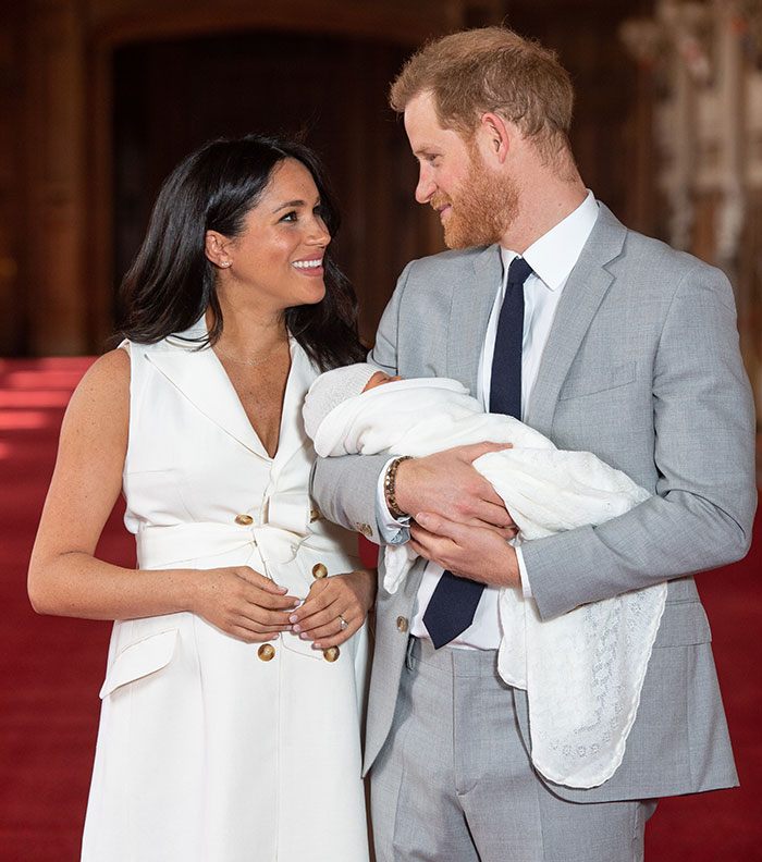 Royals with baby, smiling warmly, Meghan Markle holding their child.