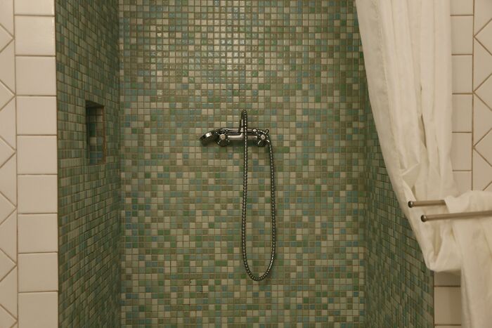 Shower with green mosaic tiles, lacking practicality despite aesthetic appeal, illustrating vessel sinks' impracticality.