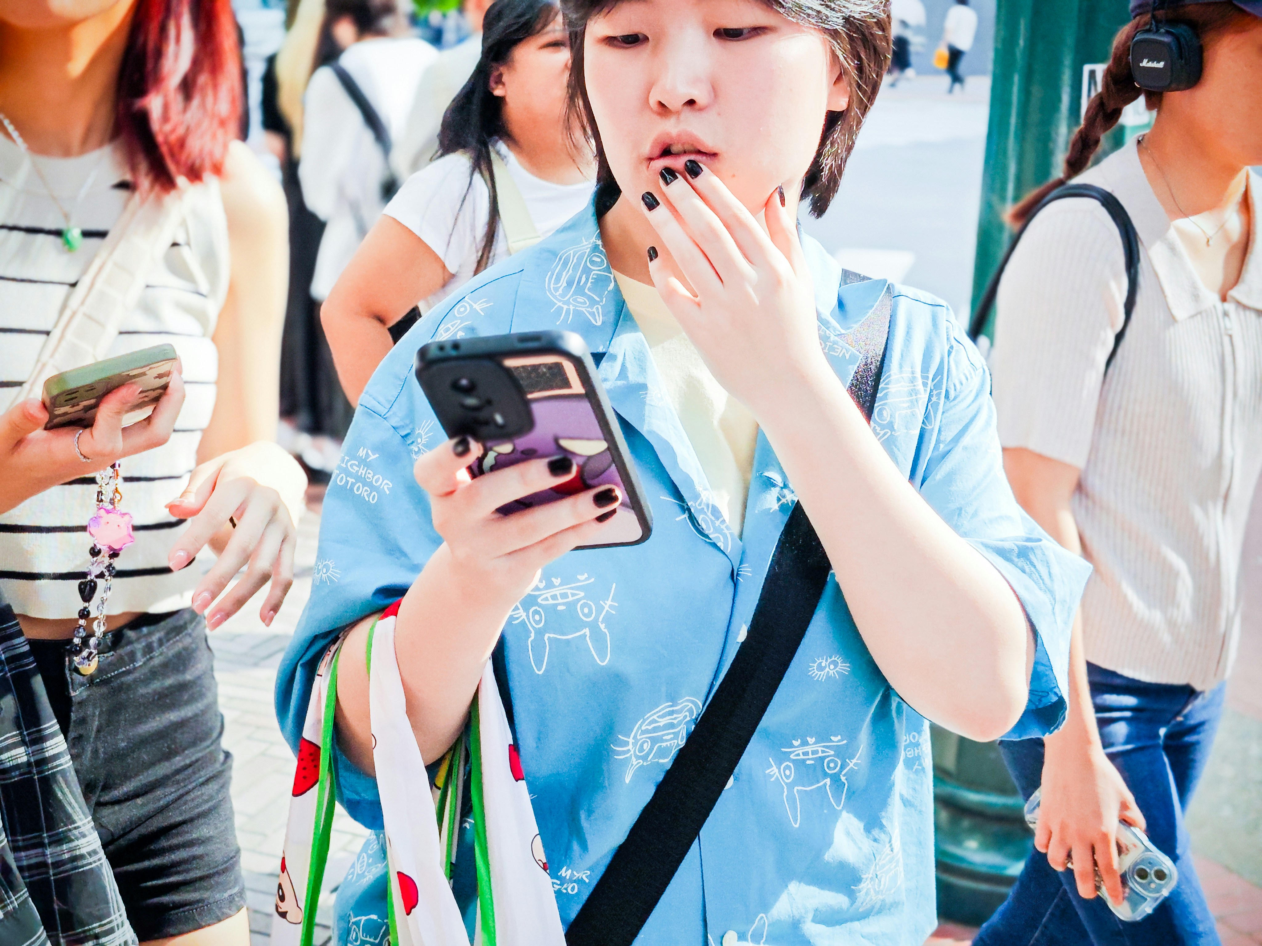 Woman in a blue shirt holding an expensive phone case while walking in a crowd outdoors.