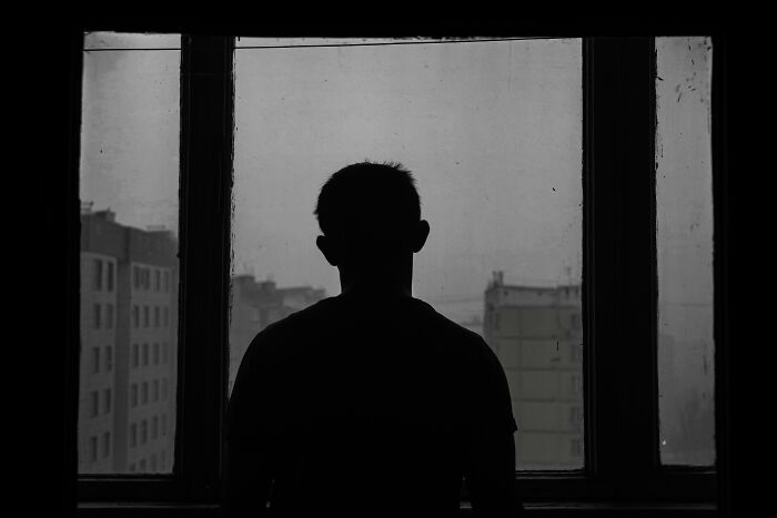 Silhouette of an elder millennial looking out a window at a gloomy cityscape, symbolizing 2008 recession impact.