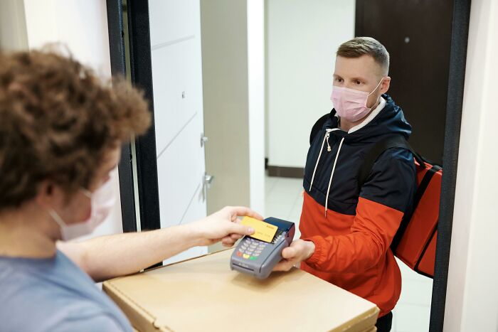 Delivery person in a mask using a card reader with a customer.