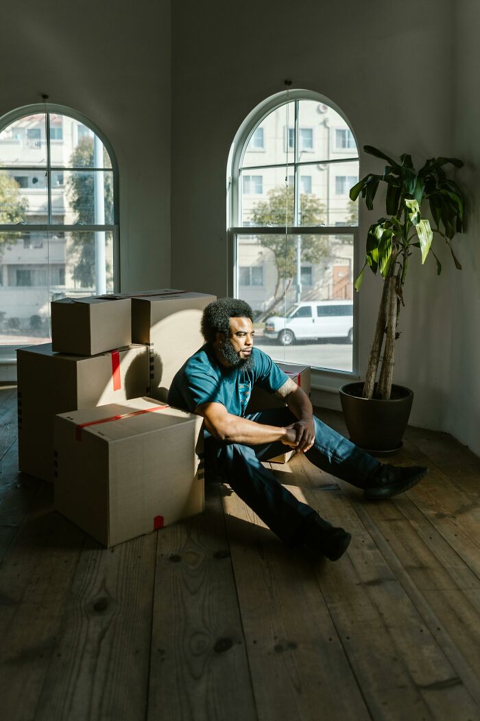 Man sitting on a wooden floor surrounded by moving boxes, representing elder millennials impacted by the 2008 recession.