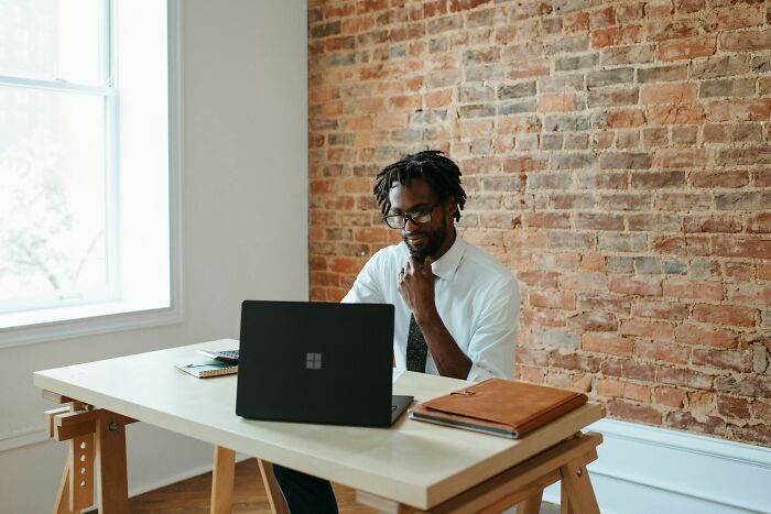 Person working on a laptop in a brick-walled office, reflecting on the 2008 recession's impact on elder millennials.