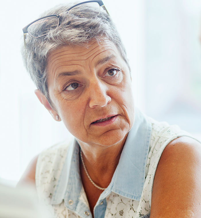 Elderly woman with short gray hair and glasses, contemplating financial planning for her parents' apartment share.