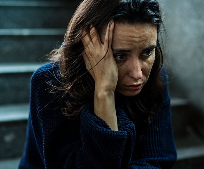 A woman appearing distressed, holding her head while sitting on stairs, reflecting on money and family apartment share issues.