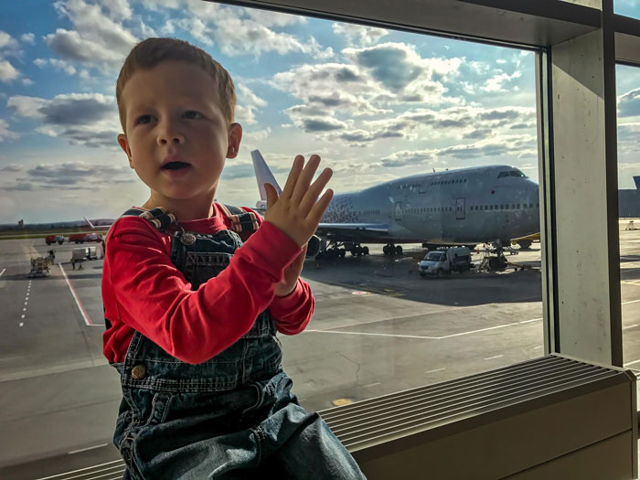 Young boy sitting by airport window with airplane outside, symbolizing mom planning trip to Europe with son.