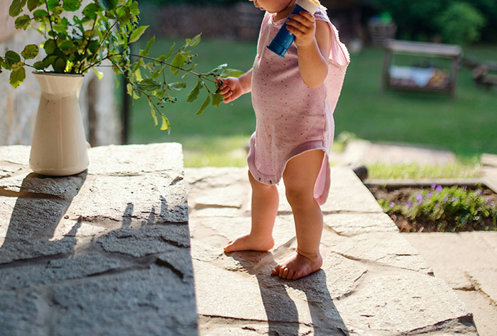 Baby in pink outfit holding a toy outside on stone steps next to a plant, symbolizing parenting moments.