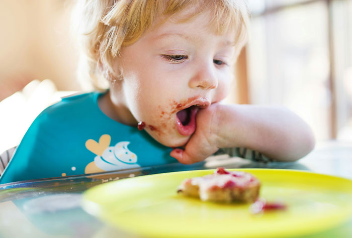 A child eating messily at a table, wearing a colorful bib, represents stories of moms shamed by strangers.
