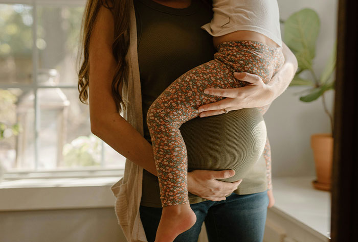 Mother holding child near window, showcasing parental bond and challenges with strangers’ judgment.