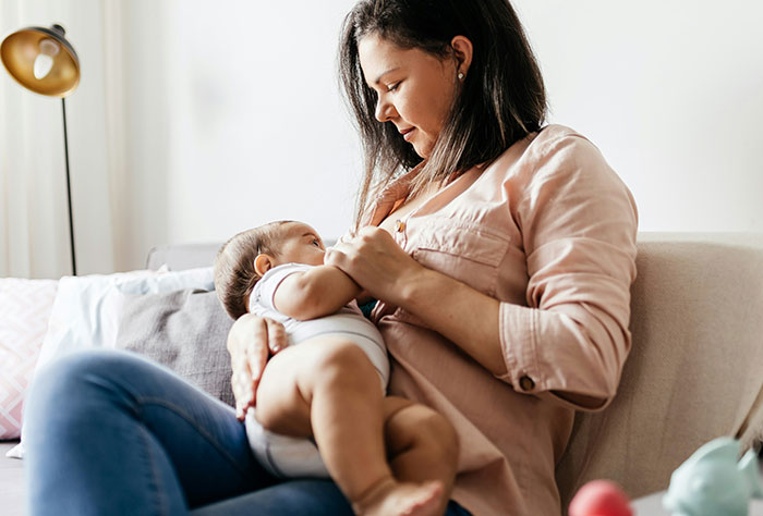 Mother breastfeeding baby on a couch, reflecting real-life moments of moms facing public scrutiny.