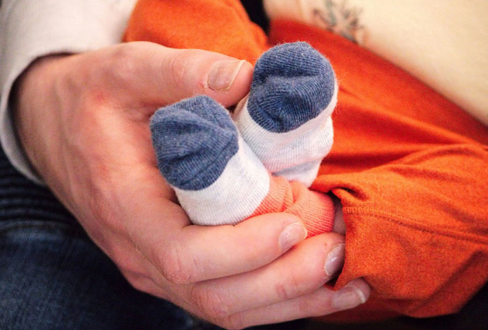 A parent holding a baby in orange clothing, focusing on tiny socked feet, highlighting a tender moment.