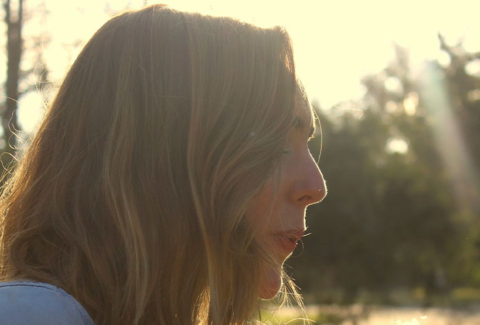 A thoughtful mom outdoors, sunlight highlighting her face, reflecting on experiences with strangers.