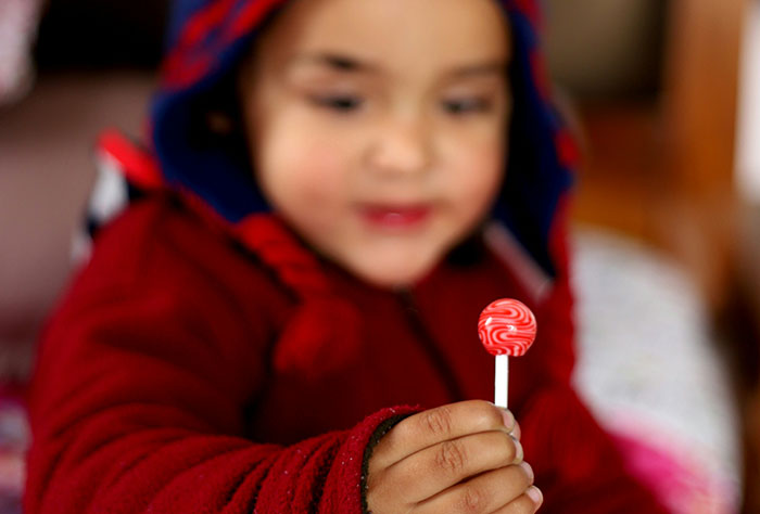 Child in a red jacket holding a red lollipop, illustrating themes of mom shaming by strangers.