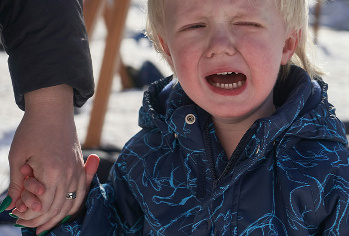 Child in blue jacket crying while holding an adult's hand, illustrating a moment of mom shaming.