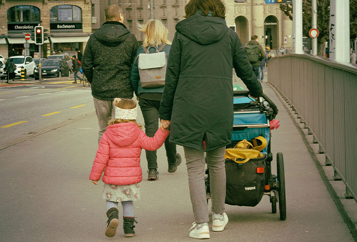 Mom pushing stroller, holding child's hand in urban setting, highlighting experiences of moms getting shamed by strangers.