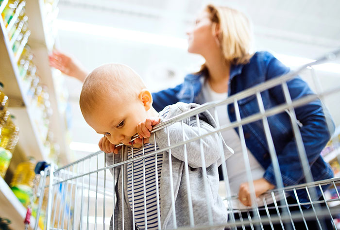 Baby in shopping cart while mom shops in grocery store aisle.