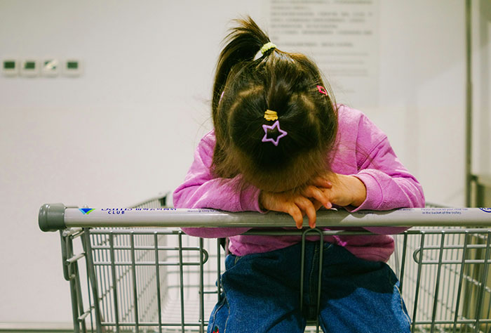 Child resting on shopping cart in a store, wearing a pink jacket, relevant to stories about moms being shamed by strangers.