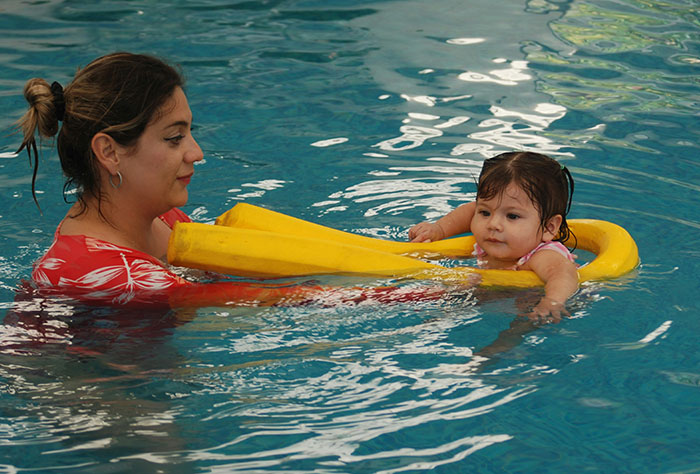 Mom teaching her toddler to swim in a pool, showcasing parenting moments.