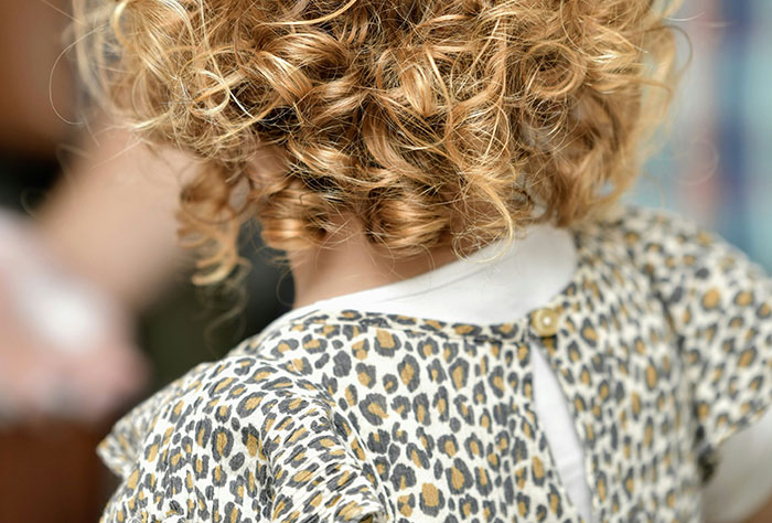 Child with curly hair wearing a leopard print dress, illustrating stories about moms getting shamed by strangers.