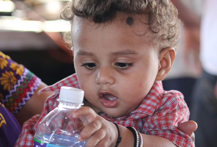 Toddler in plaid shirt holding water bottle, symbolizing stories about moms facing shaming by strangers.