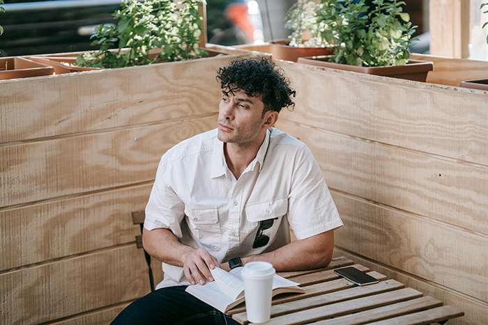 Young man sitting at a wooden table with a book and coffee, reflecting on mom stealing his college fund cash.