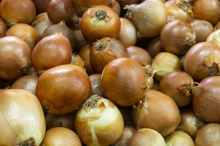 A pile of fresh onions, displaying their brown skins and papery texture, commonly seen in grocery stores.