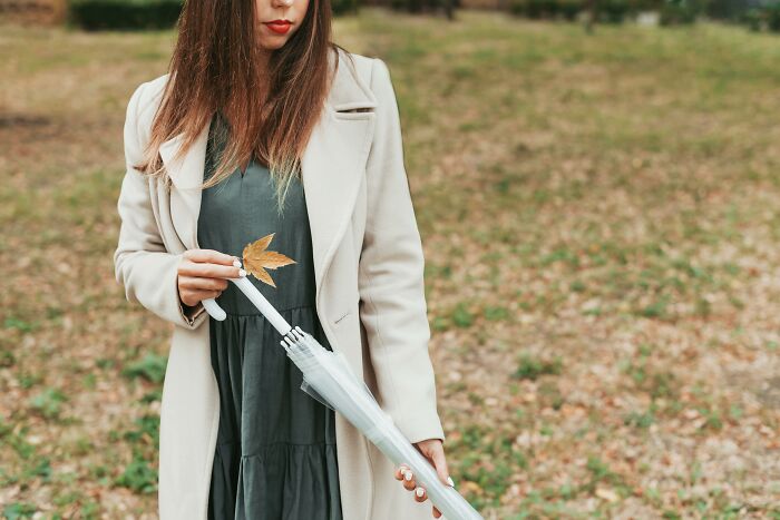 Woman in a coat holding a leaf and umbrella outdoors, an example of cringiest things people do in public.