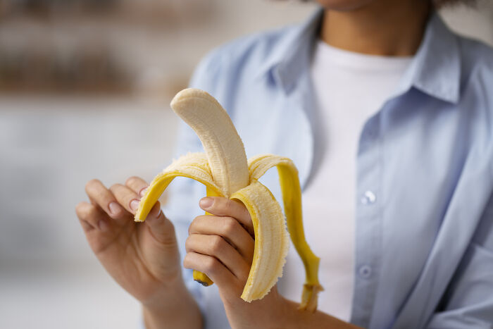 Person in a blue shirt peeling a banana casually, focusing on the fruit.