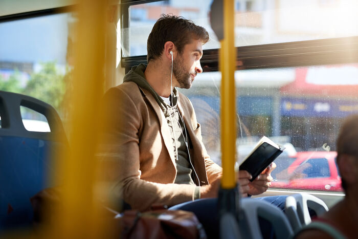 Man on a bus wearing earphones, reading a tablet, unaware of cringiest moments happening around him.