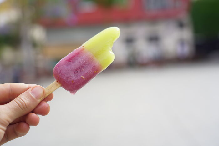 A hand holds a partially melted, two-tone popsicle in a public space, capturing a cringey moment.