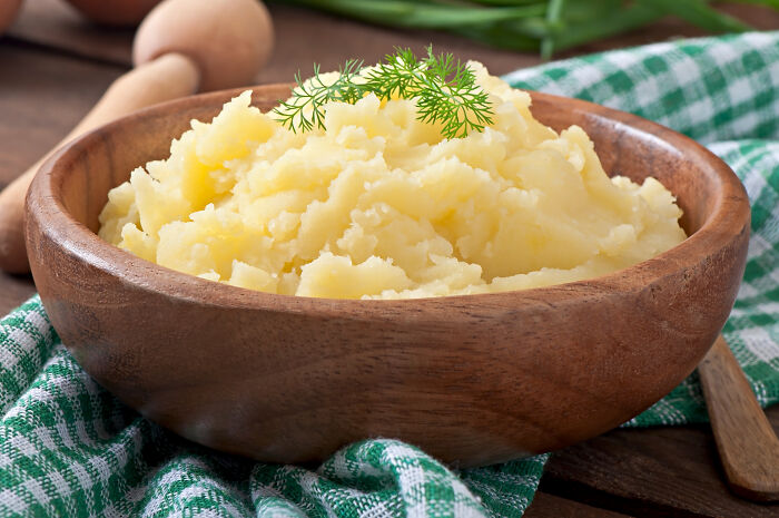 Mashed potatoes in a wooden bowl on a checkered cloth, garnished with dill.