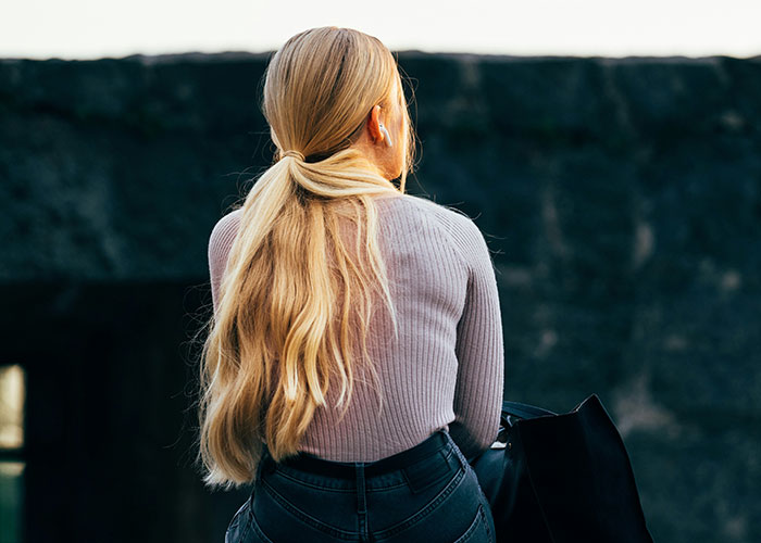Woman with long blonde hair in casual attire, sitting outdoors, headphones in, embodying family dynamics theme.