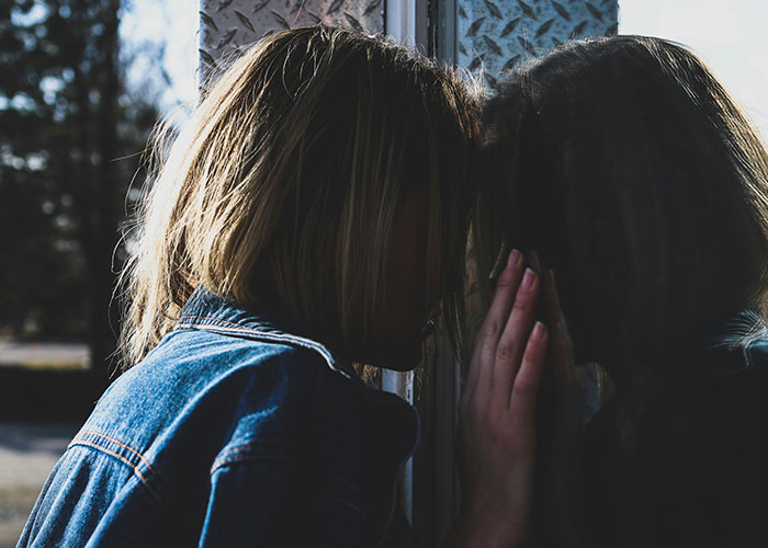 Person leaning against a reflective surface, obscuring their face, wearing a denim jacket, symbolizing unhinged emotions.