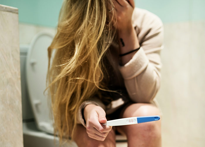A distressed woman holding a pregnancy test, sitting in a bathroom, highlighting family-related issues.