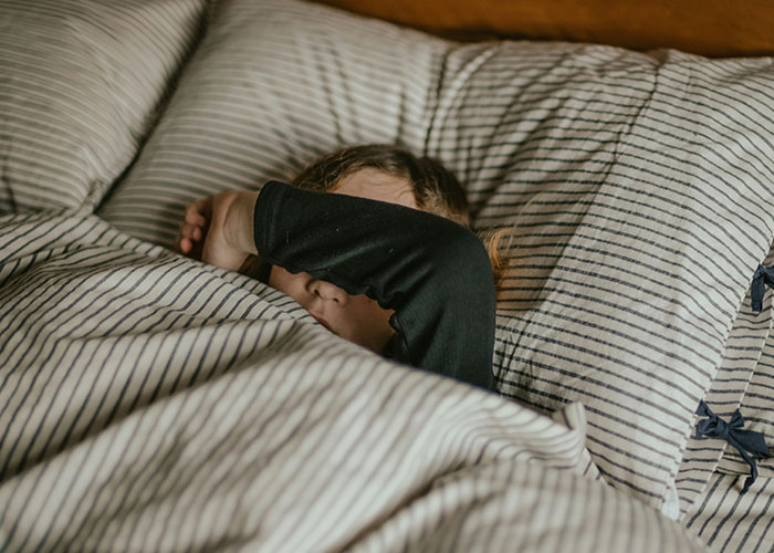 Child lying in bed with arm over face, illustrating unhinged family dynamics.