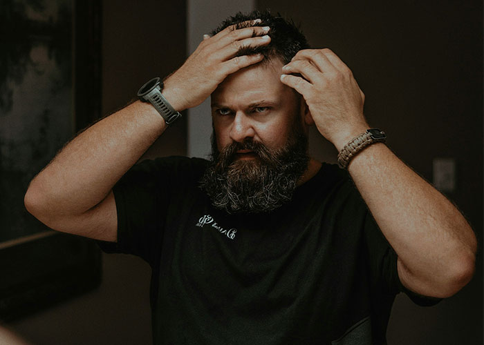 Man adjusting hair in dimly lit room, conveying concern; example of unhinged family actions.