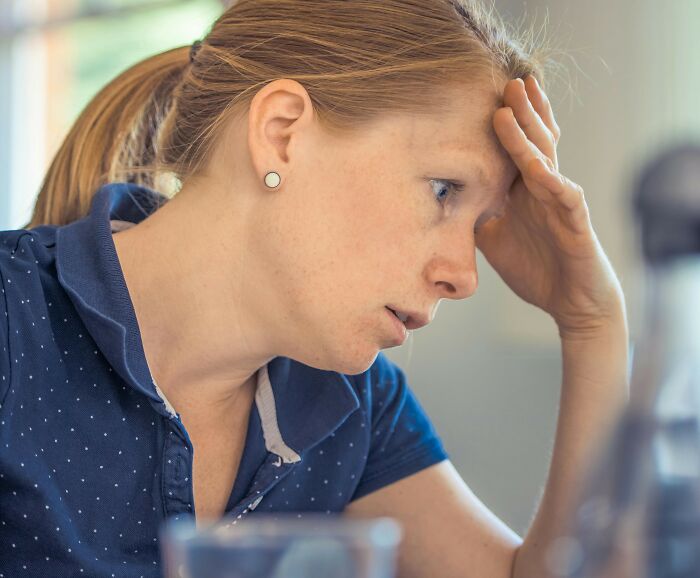 A concerned woman in a blue shirt, reacting to being excluded from play dates, highlighting mean girl behavior among moms.