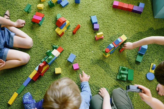 Children play with colorful blocks on green carpet; moms not inviting others for play dates.