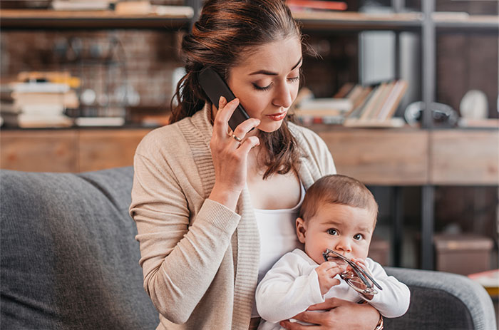 Woman on maternity leave holding baby while taking a phone call, highlighting work-life balance challenges. Woman on maternity leave holding baby while taking a phone call, highlighting work-life balance challenges.
