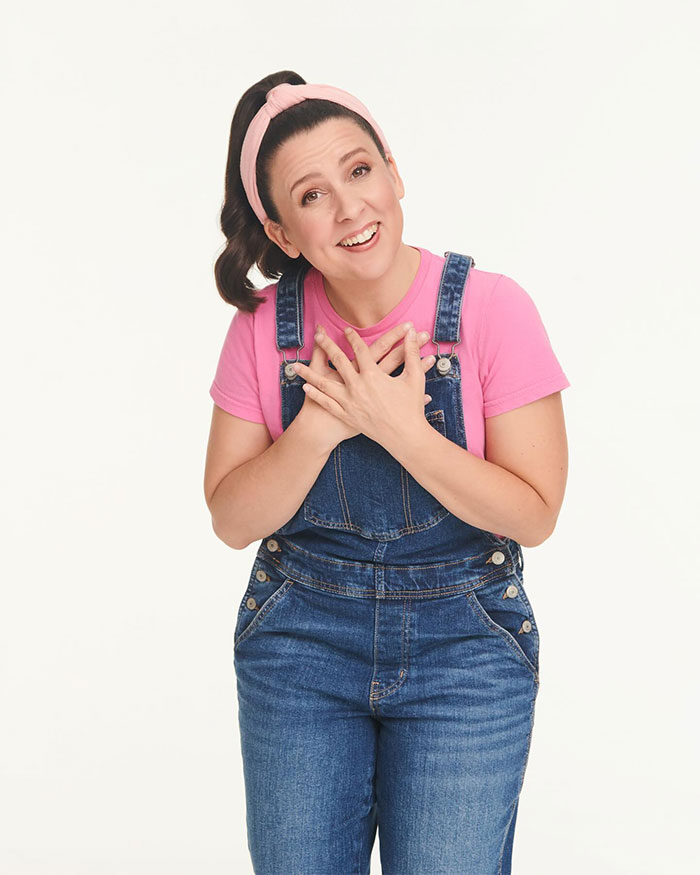 Ms. Rachel in pink top and denim overalls, hands on chest, illustrating net worth success.