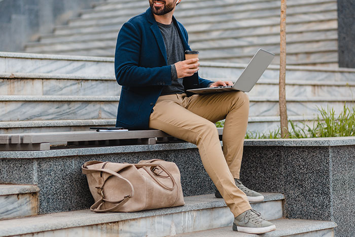 Man with laptop and coffee sitting outdoors on stairs, showcasing a casual work setting.